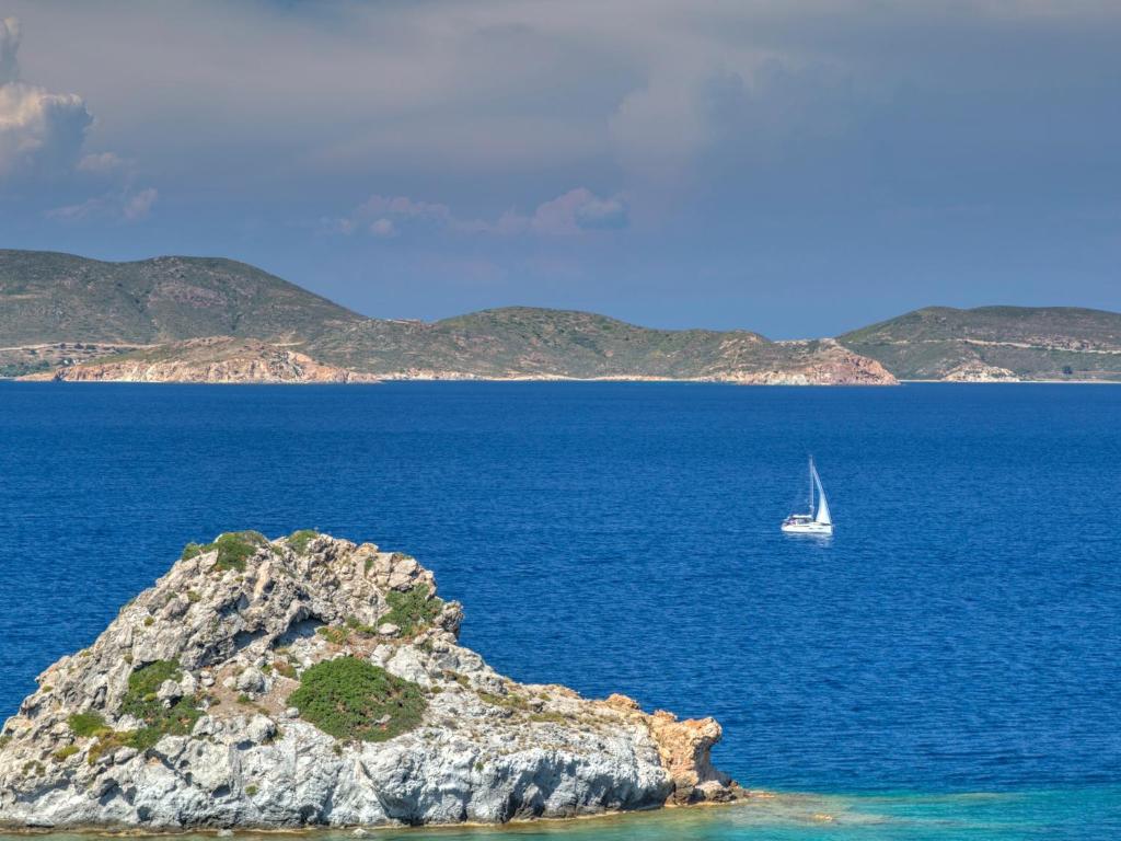 a sailboat in the ocean next to a small island at Eirini Luxury Hotel Villas in Grikos