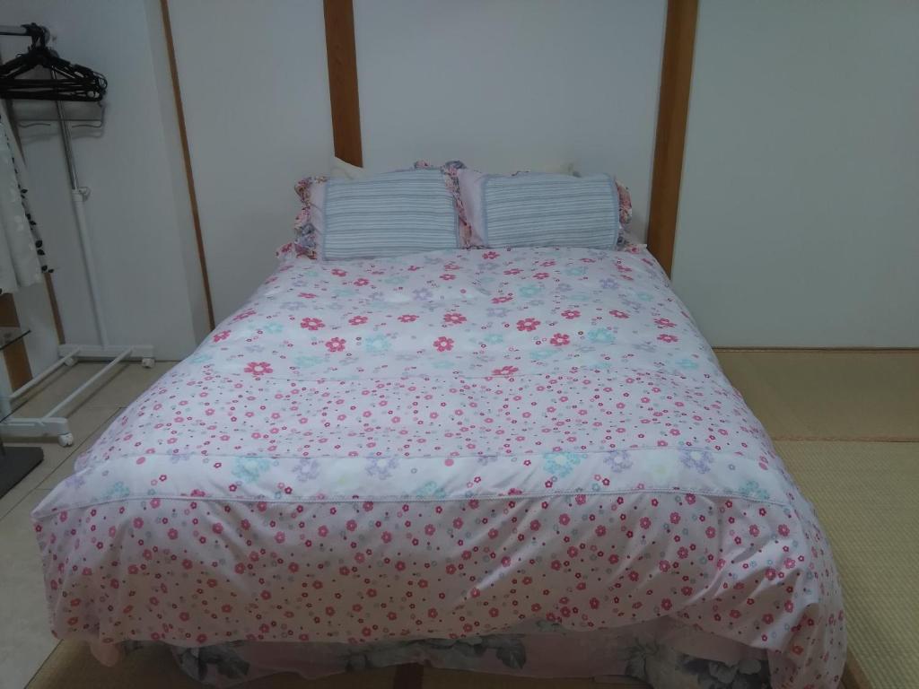a bed with a pink bedspread with flowers on it at Osaka Kuma House in Osaka