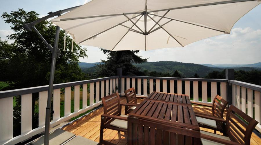 una terraza de madera con mesa y sombrilla en Bergoase Panorama-Apartments, en Kirnitzschtal