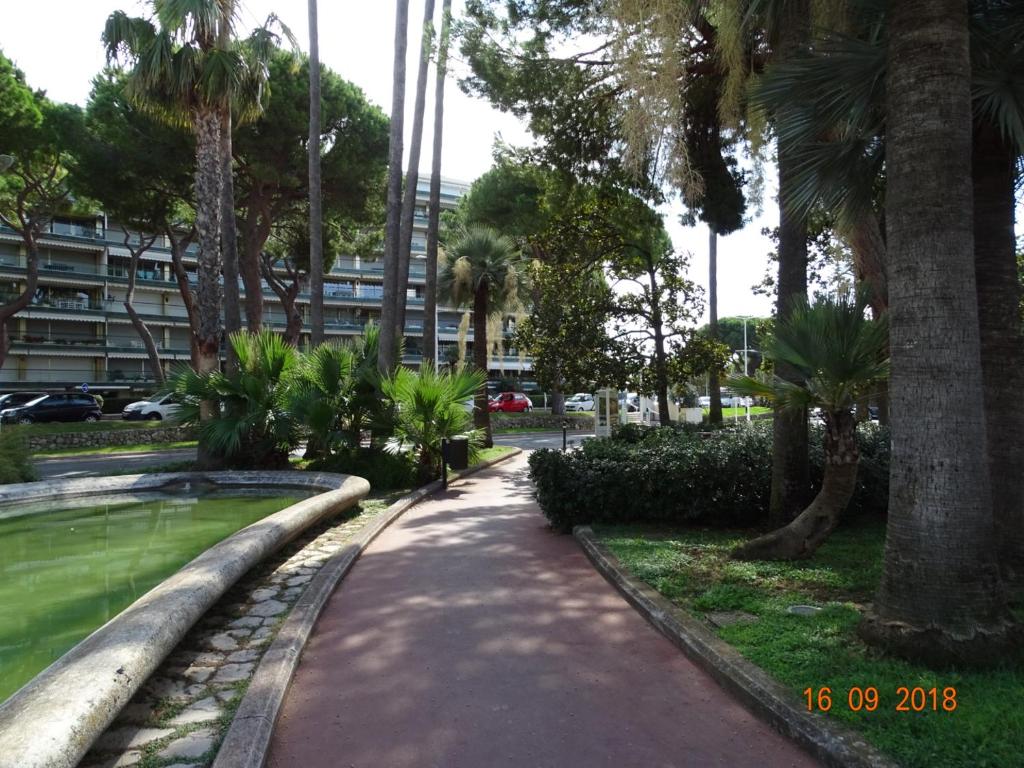 a walkway in a park with palm trees and a building at Palm beach Cannes Azur in Cannes