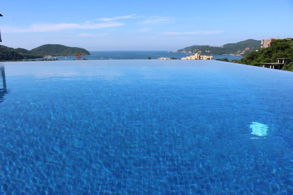 a large blue swimming pool with the ocean in the background at Sunset House Zihuatanejo in Zihuatanejo