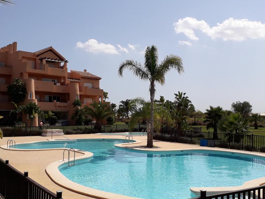 einem Pool mit einer Palme vor einem Gebäude in der Unterkunft Mar Menor Golf Resort Rental in Torre-Pacheco