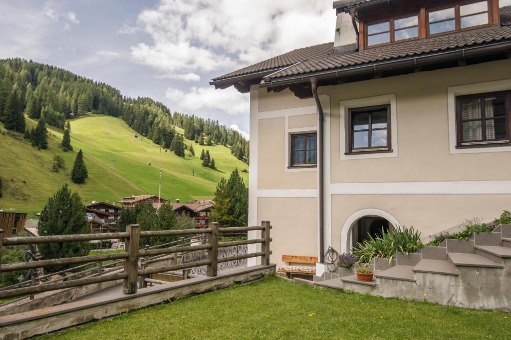 a house with a fence next to a green hill at Casa Matie in Selva di Val Gardena