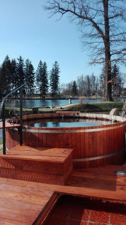 Round wooden hot tub on deck overlooking calm lake and bare trees under clear sky.
