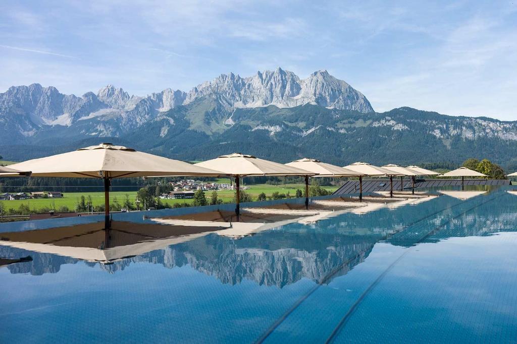 una fila de sombrillas sentadas junto a una piscina con montañas en Hotel Penzinghof, en Oberndorf in Tirol