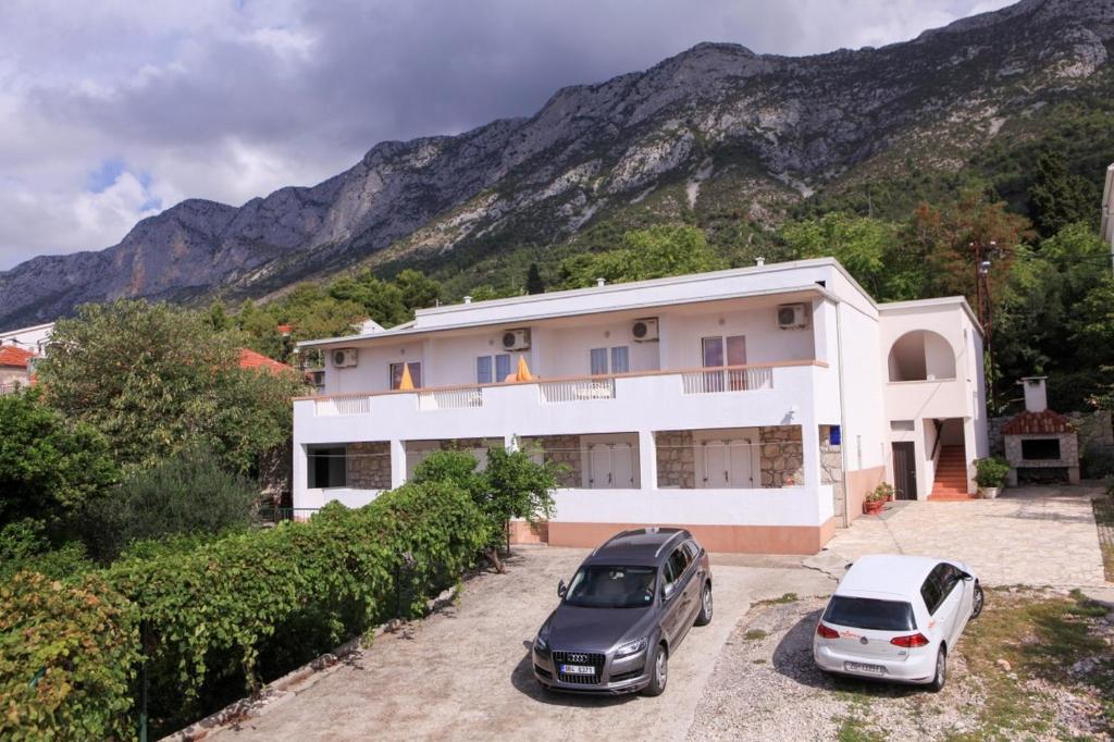 two cars parked in front of a house with mountains in the background at Apartments Duki in Gradac