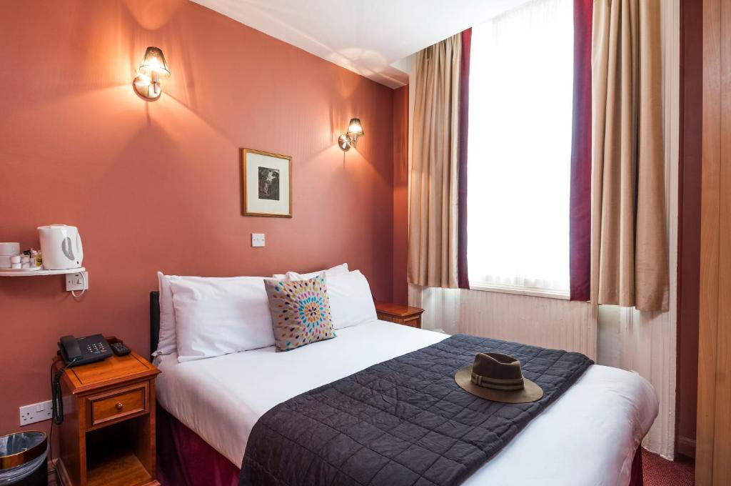 una habitación de hotel con una cama con sombrero en Park Avenue Inn Craven London Hyde Park, en Londres