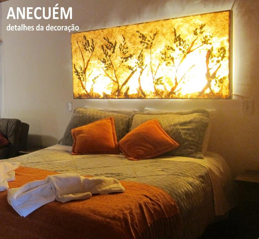 a bedroom with a bed with a painting on the wall at Pousada Anecuém in Monte Verde