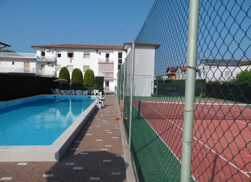une clôture à côté d'un court de tennis avec une piscine dans l'établissement Katy Apartment, à Lido di Jesolo