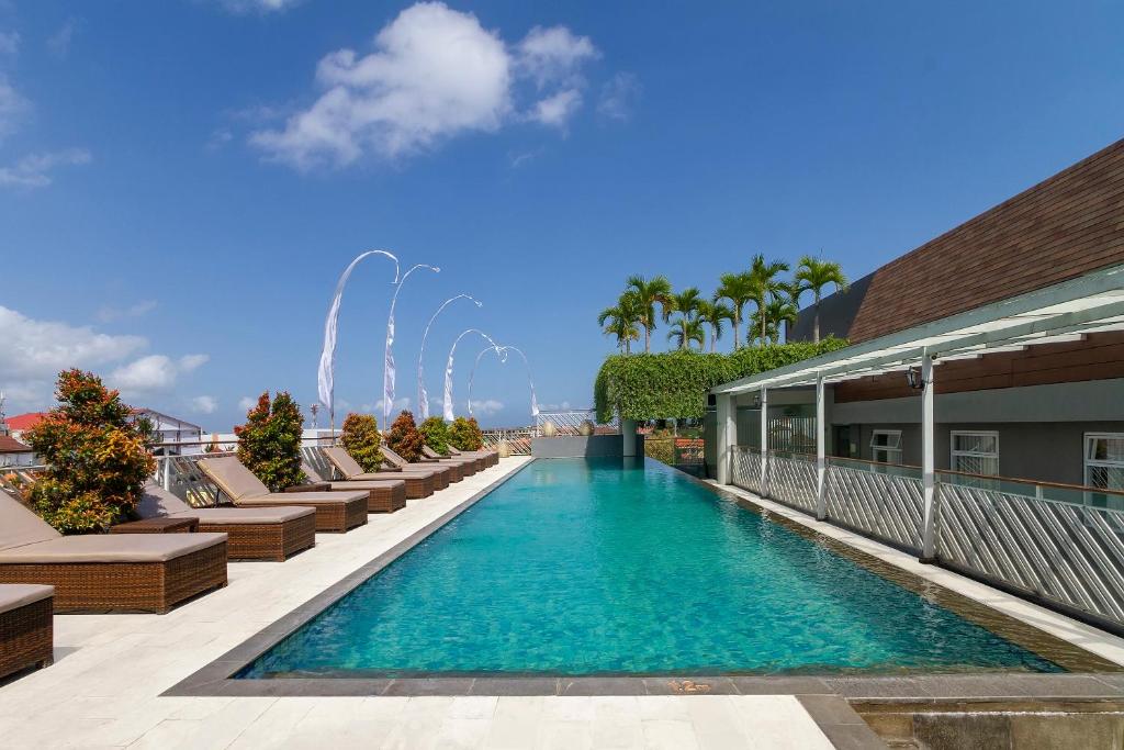 a pool on the roof of a building with chairs and a fountain at PrimeBiz Hotel Kuta in Kuta
