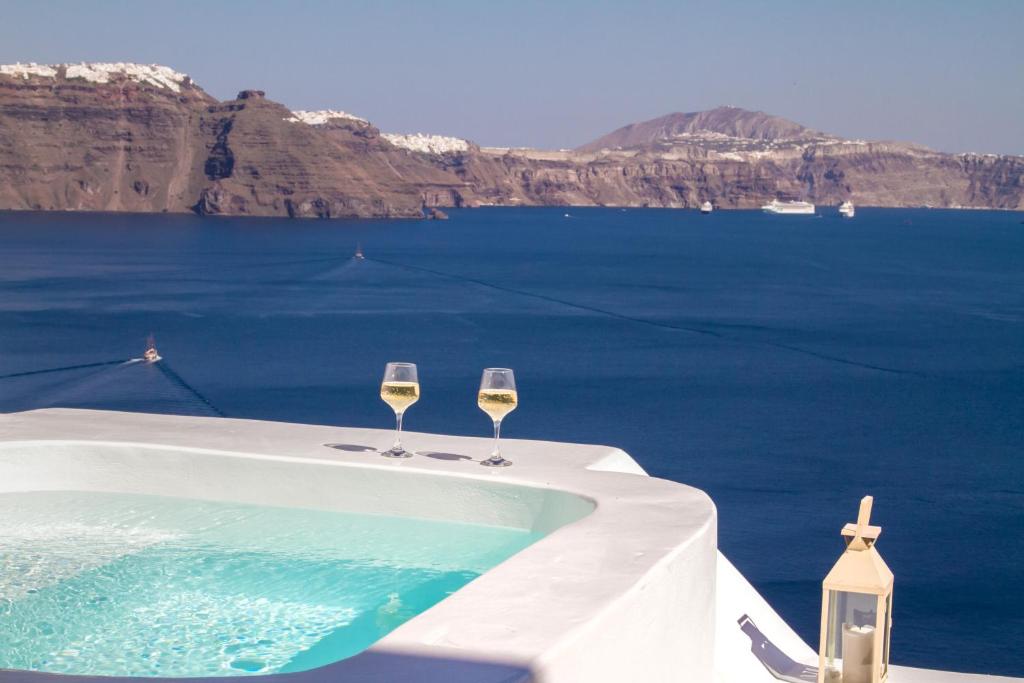 twee glazen wijn zittend op een tafel naast een zwembad bij Hector Cave House in Oia
