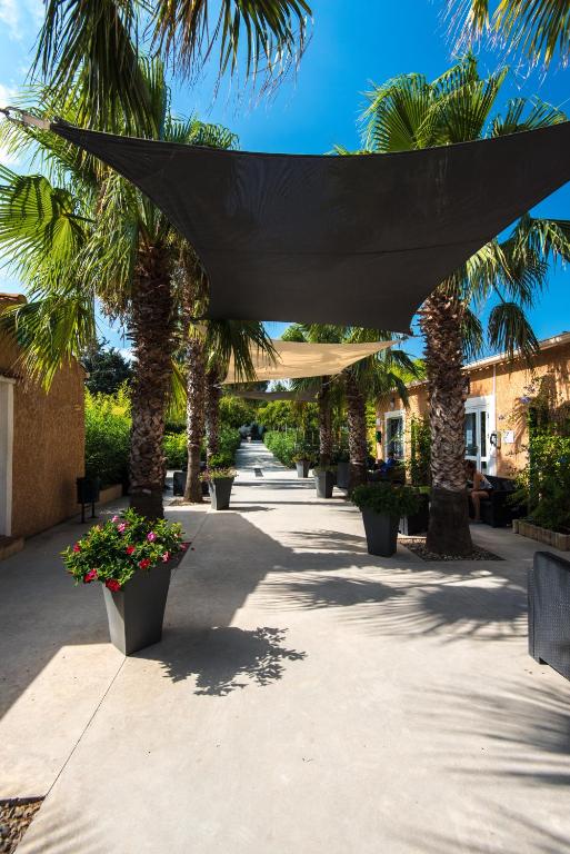 a shady walkway with palm trees and plants at Domaine La Pinède Enchantée in Argelès-sur-Mer