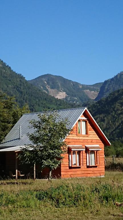 ein Holzhaus auf einem Feld mit Bergen im Hintergrund in der Unterkunft Coñaripe Kuyen Mapu Cabañas in Coñaripe