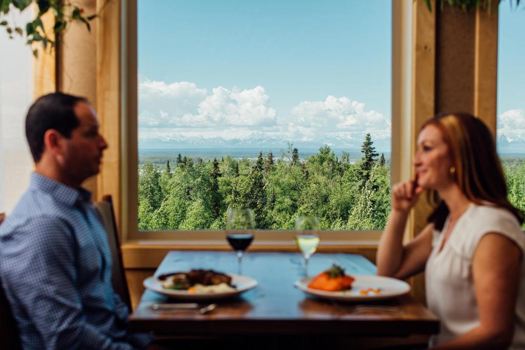 Um homem e uma mulher sentados à mesa com comida. em Talkeetna Alaskan Lodge em Talkeetna