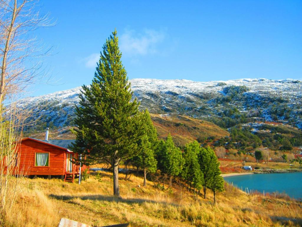 a red cabin on a hill next to a lake at La Lomita Guadal in Puerto Guadal