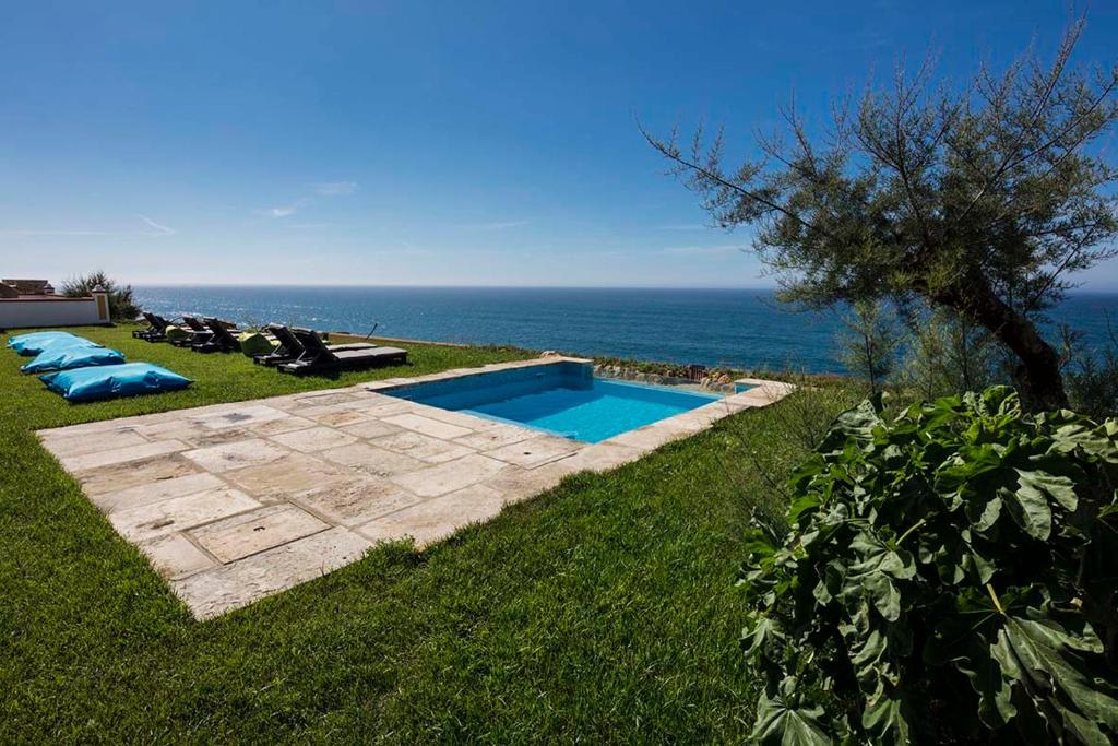 a swimming pool in the grass next to the ocean at Chalet O Amorzinho Sintra Praia in Sintra