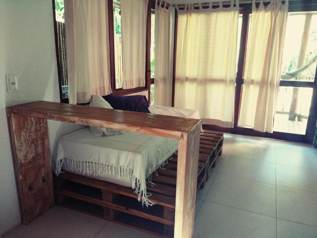 a bed with a wooden frame in a room with windows at Vila Engawa Flats in Itacaré