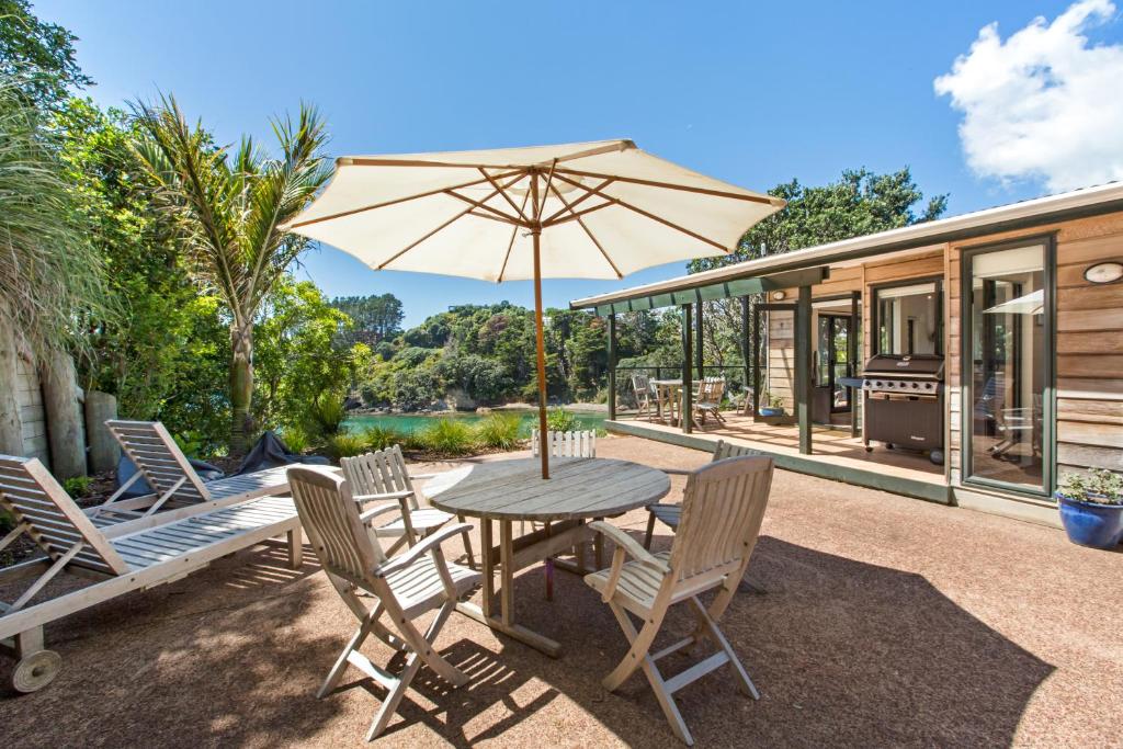 a patio with a table and chairs and an umbrella at Beachfront Enclosure Bay - Waiheke Unlimited in Oneroa