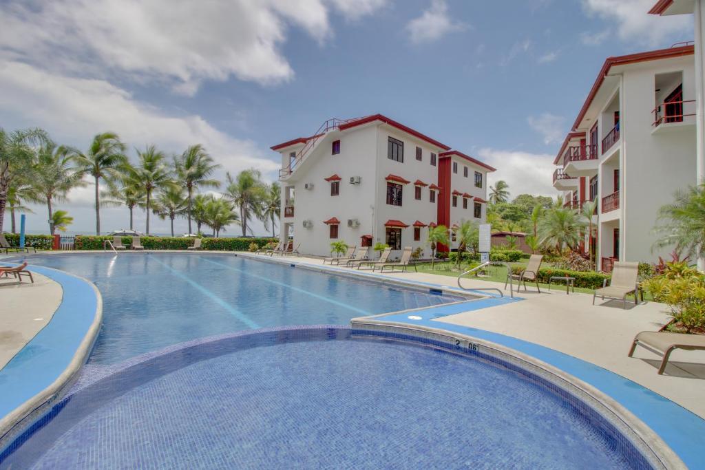 Una piscina en un resort con sillas y palmeras. en Bahia Azul 7A, en Jacó