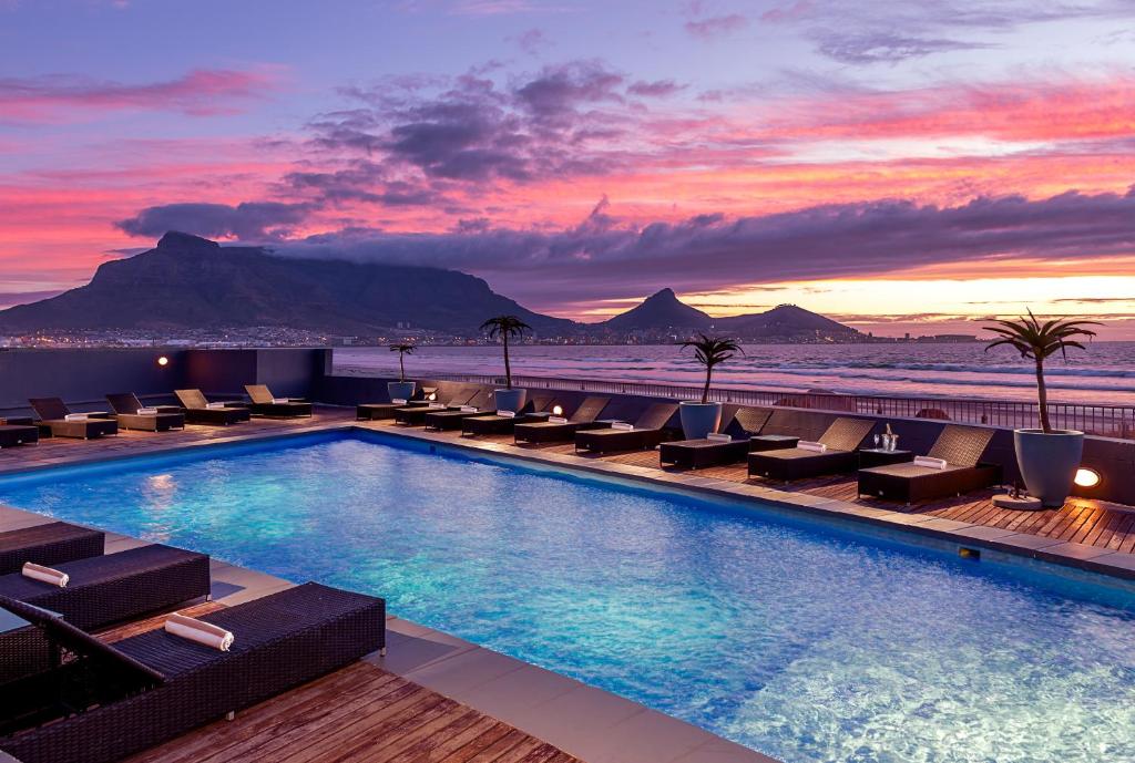 a hotel pool with chairs and a sunset at Lagoon Beach Hotel Apartments in Cape Town