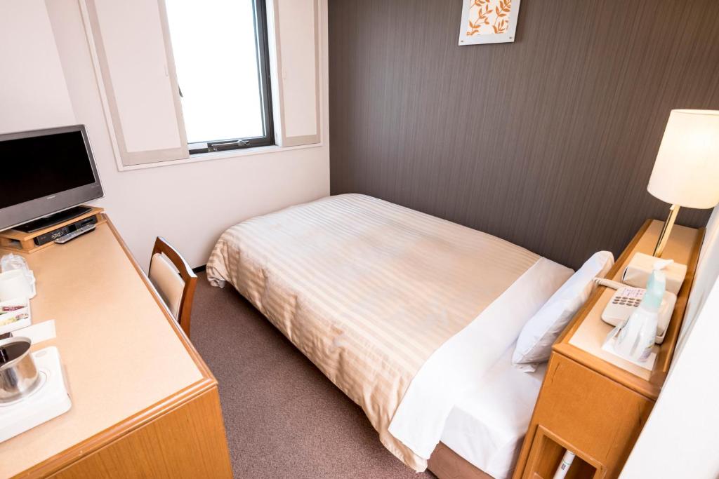 a small room with a bed and a desk and a television at Hashimoto Park Hotel in Sagamihara