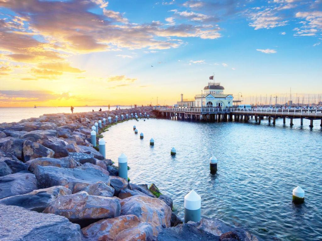 a pier with a lighthouse in the water at sunset at Beachfront Apartment in Melbourne