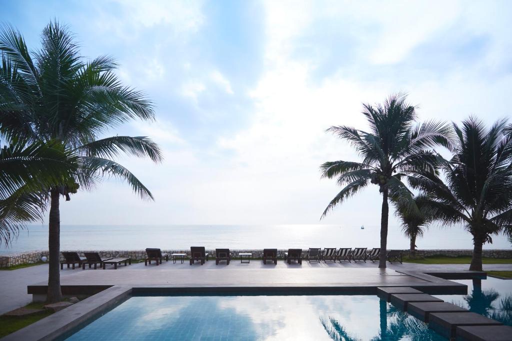 a resort swimming pool with palm trees and the ocean at Siambeach Resort in Cha Am