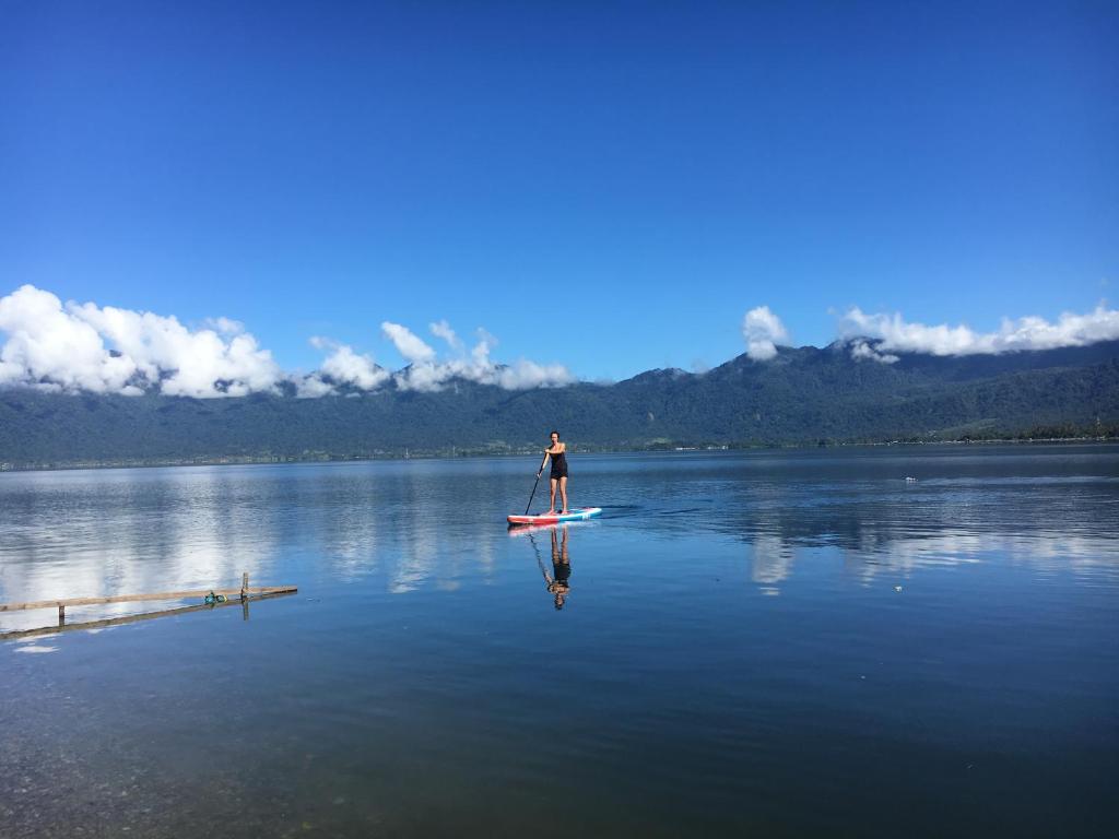 a man standing on a paddle board on a lake at Eka's Bungalows in Maninjau