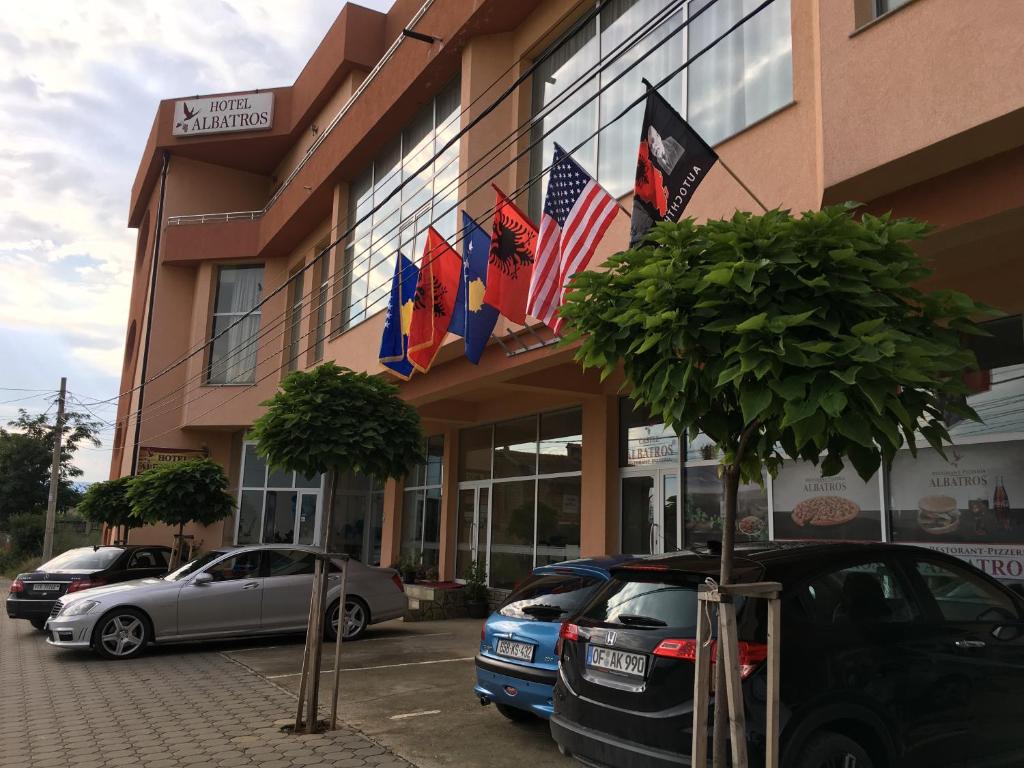 a building with flags and cars parked in front of it at Hotel Albatros in Prizren