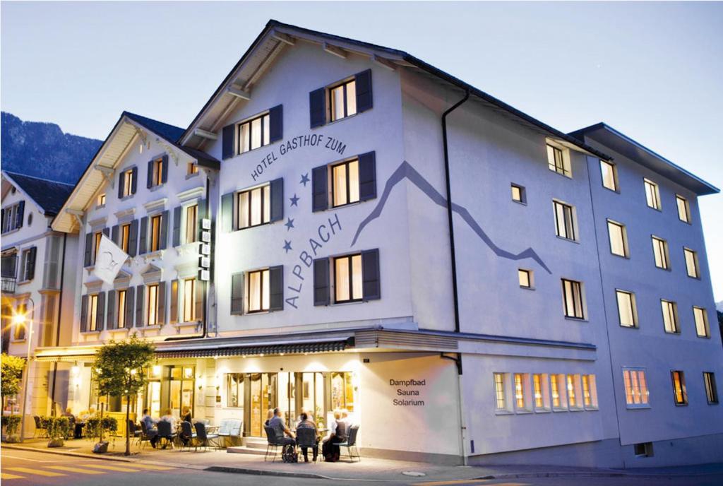eine Gruppe von Personen, die außerhalb eines Gebäudes sitzen in der Unterkunft Hotel Alpbach in Meiringen