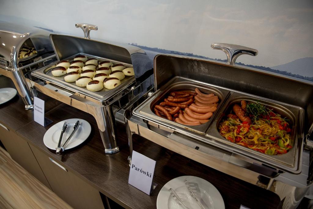 Hot buffet chafing dishes holding sausages and sautéed peppers beside plates and serving tongs.