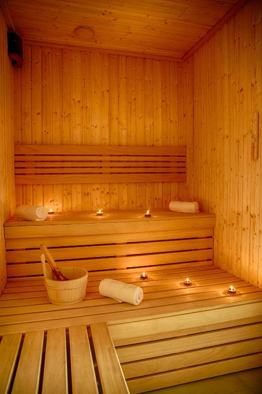 Cozy wooden sauna bench view with tea-light candles, rolled towels, and wooden water bucket.