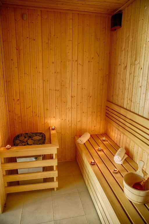 Wood-paneled sauna with wooden benches, rolled towels, candlelight, sauna bucket and ladle, warm cozy atmosphere.