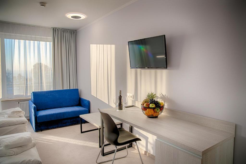 Sunny hotel sitting area with desk, fruit bowl, wine bottle, blue sofa and window.
