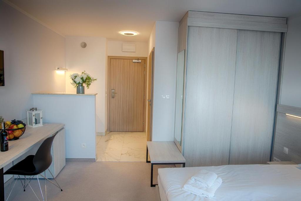 Bright hotel room entryway with bed, folded towels, wardrobe, desk with fruit and wine.
