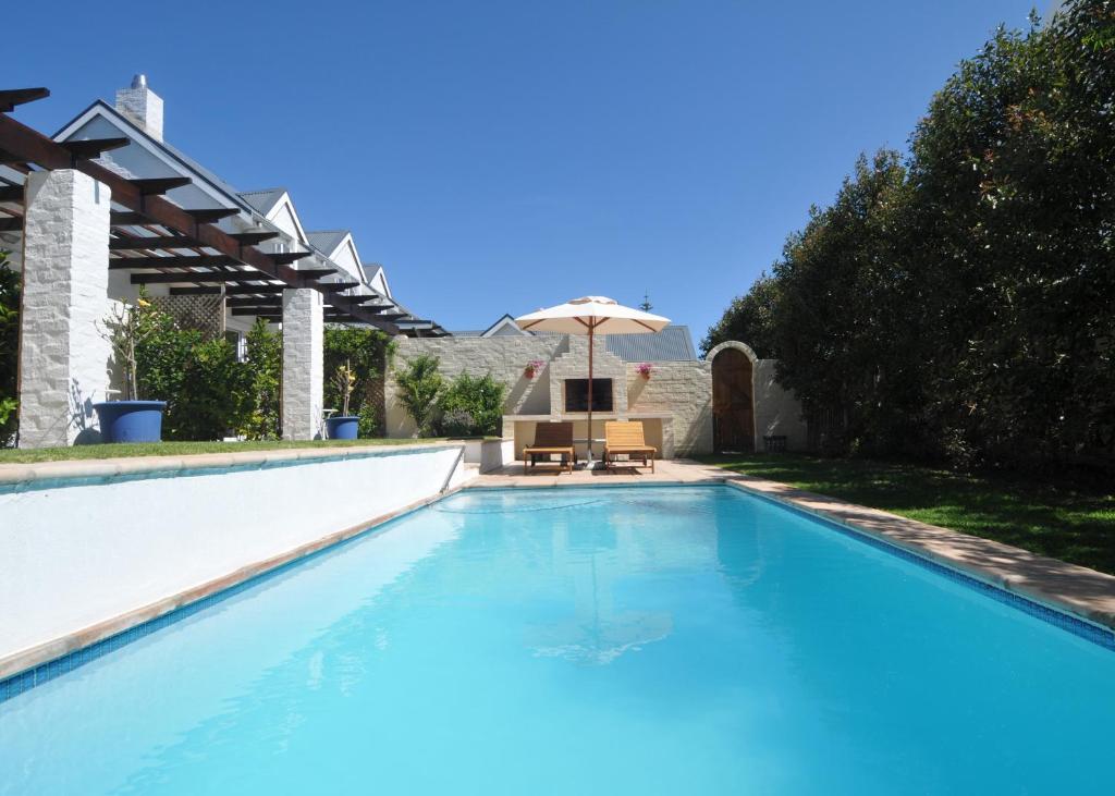 a swimming pool with an umbrella and a chair at The Gables Hermanus in Hermanus