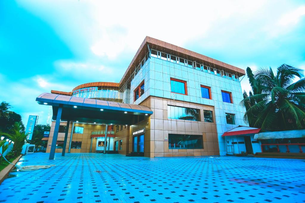 a building with a palm tree in front of it at Hotel White City in North Paravur