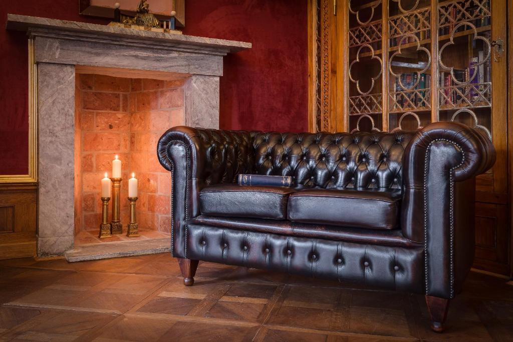 Dark leather Chesterfield sofa beside glowing candles in stone fireplace, book on seat, cozy library mood