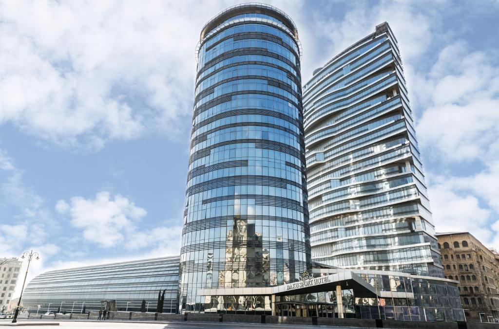 um edifício de vidro alto com uma torre de relógio em frente em Sahil Hotel Baku em Baku