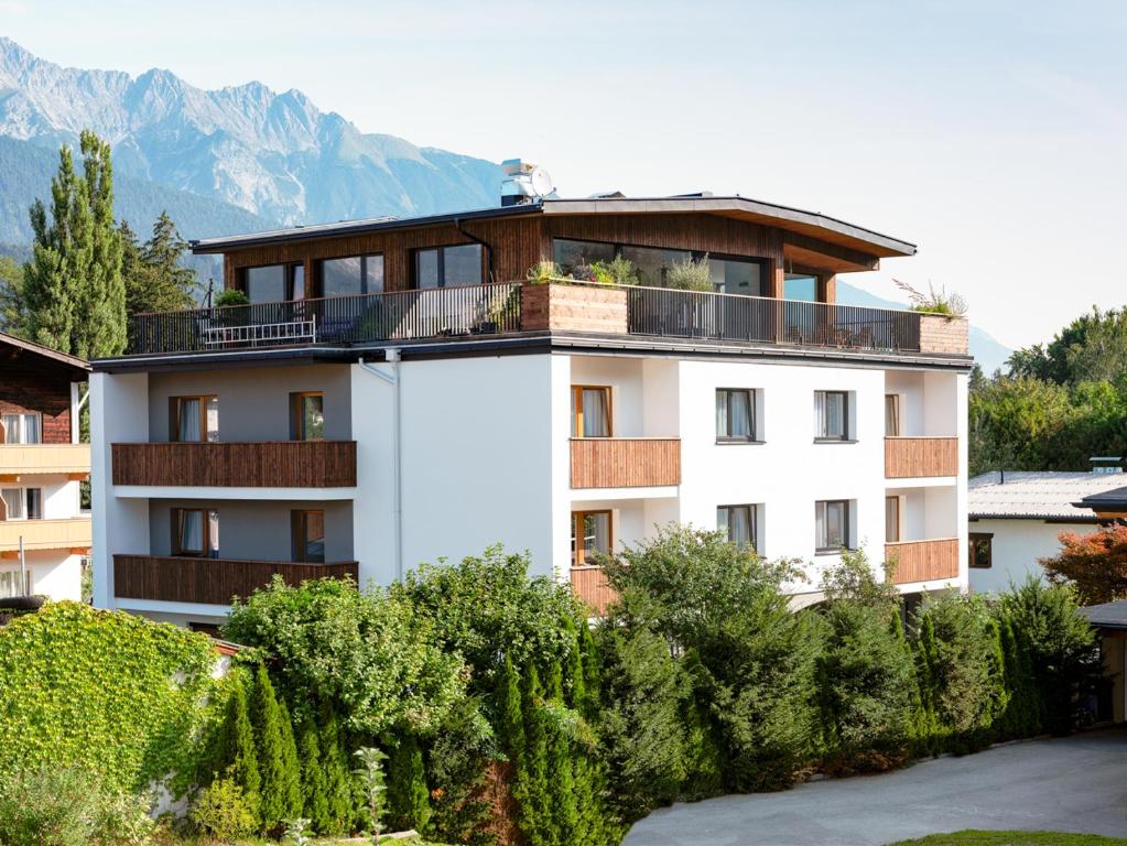 ein weißes Apartmenthaus mit Bäumen und Bergen im Hintergrund in der Unterkunft Pension Clara in Wattens