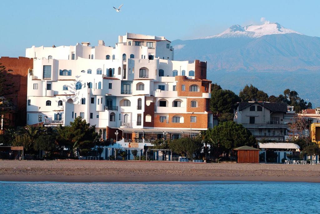 een groot wit gebouw bovenop een strand bij Sporting Baia Hotel in Giardini Naxos