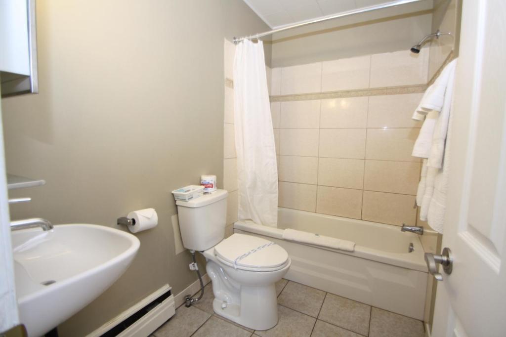 a bathroom with a toilet and a tub and a sink at Harrison Spa Motel in Harrison Hot Springs