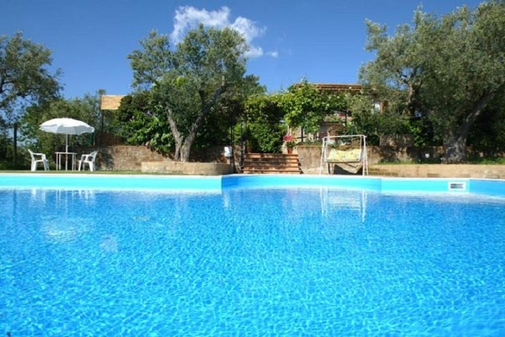 a large blue swimming pool with a table and an umbrella at Maremma Nel Tufo in Pitigliano