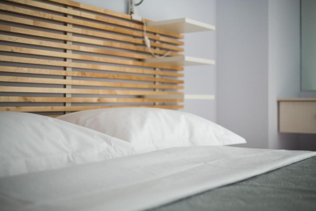 1 cama con sábanas blancas y cabecero de madera en Nephiria, Live like a local next to Acropolis!, en Atenas