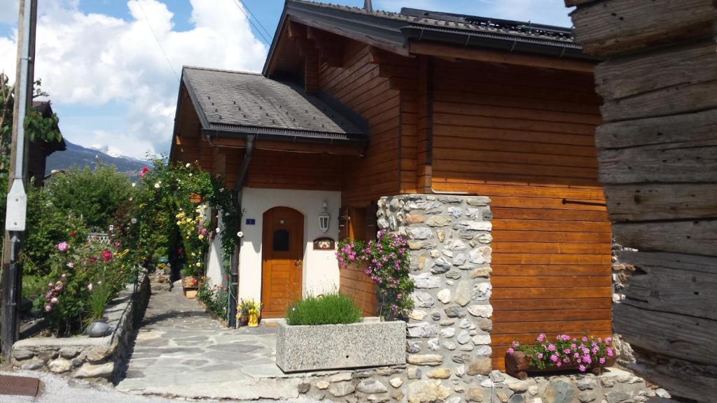 una pequeña casa de madera con flores delante en la grange à Caroline en Ayent