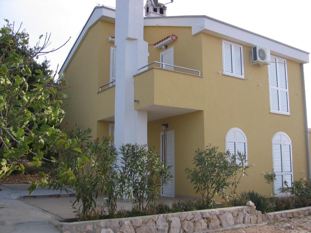 a yellow house with white shutters and trees at Apartmani Hržan-Keglević in Mandre