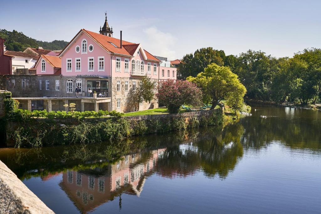 un grand bâtiment rose assis à côté d'une rivière dans l'établissement Ribeira Collection Hotel by Piamonte Hotels, à Arcos de Valdevez