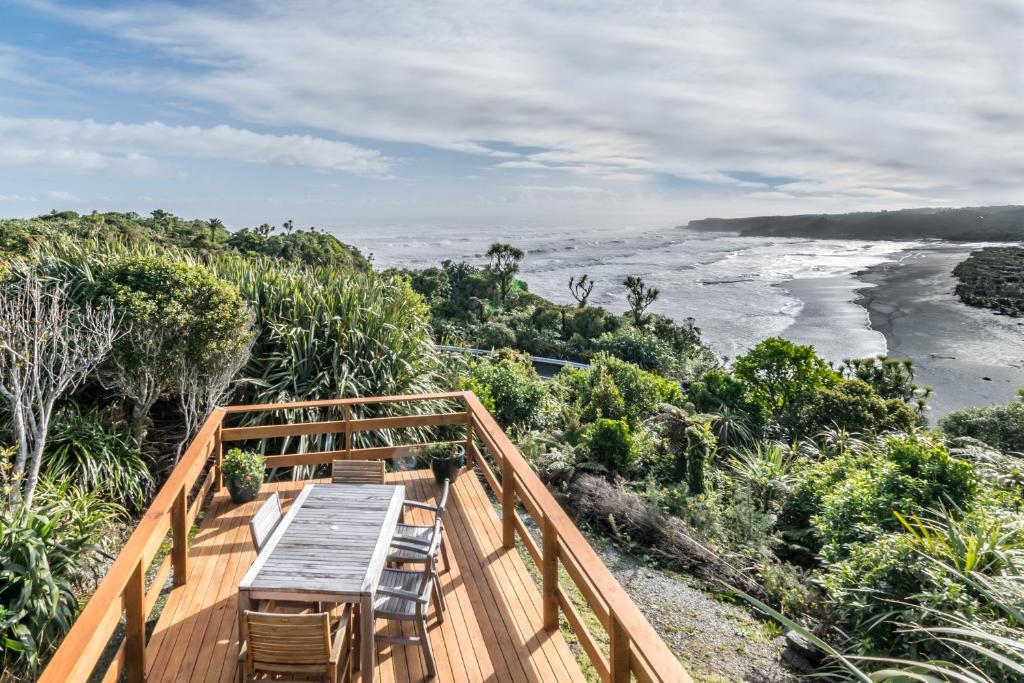 eine Holzterrasse mit einem Tisch und Stühlen sowie Meerblick in der Unterkunft Paparoa Park Motel in Punakaiki