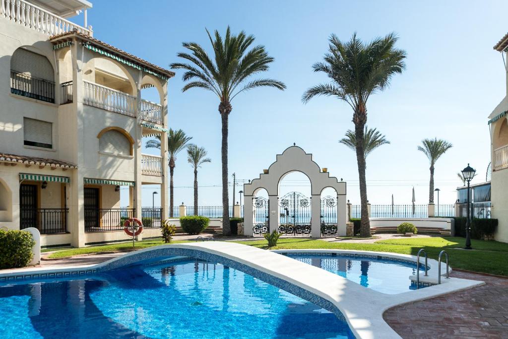 a swimming pool in front of a building with palm trees at Al Andalus Playa Muchavista El Campello in El Campello