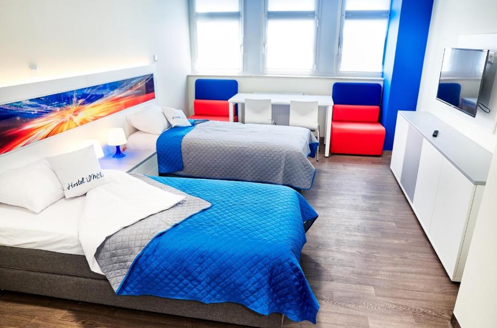 two beds in a room with two red chairs at Hostel Umed in Łódź